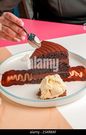 Hand taking a piece of three layered chocolate cake with cream and gelato scoop. Stock Photo