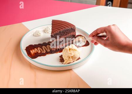 Hand taking a piece of three layered chocolate cake with cream and gelato scoop. Stock Photo