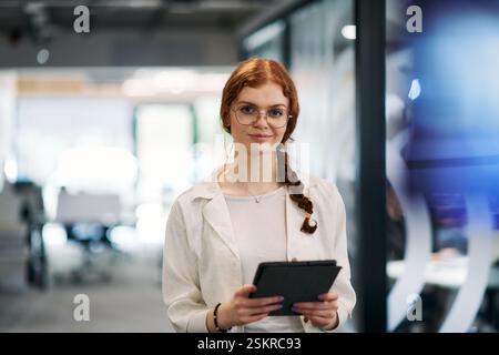 A business woman with orange hair self confident, fully engaged in working on a tablet, exuding creativity, ambition and a lively sense of Stock Photo