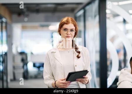 A business woman with orange hair self confident, fully engaged in working on a tablet, exuding creativity, ambition and a lively sense of Stock Photo