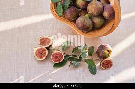 A rustic wooden bowl containing a mix of whole and halved fresh figs and feijoa, placed on a light-colored surface. Close up. Stock Photo
