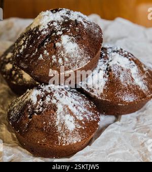Stack of chocolate muffins dusted with powdered sugar on crinkled parchment paper. Stock Photo