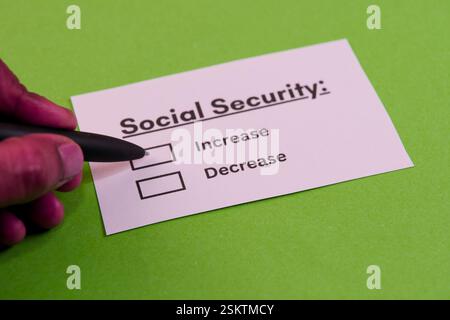Hand holding a pen, marking choices on a card about social security adjustments. Green background enhances focus. Stock Photo