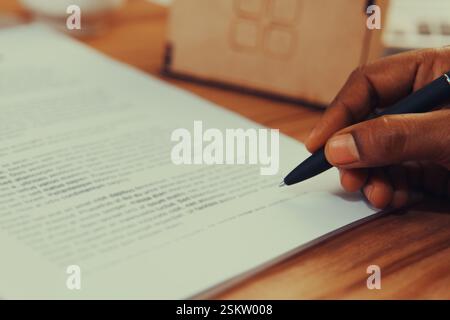 A person focuses on writing notes with a pen on a document in a warm, inviting workspace. Stock Photo