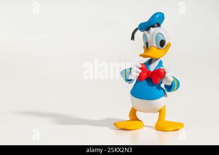 Plastic Donald Duck figurine adjusting his red bow tie, isolated on a white background, casting a shadow Stock Photo