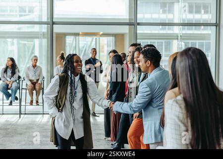 A diverse group of professionals greeting each other in a bright modern office, conveying teamwork and a positive atmosphere. Stock Photo
