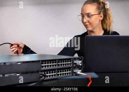 IT technician professional configuring network switch and managing network cables and hardware in a data center environment Stock Photo