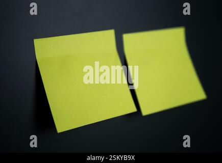 Two empty yellow sticky notes are placed on a black surface, ready for writing Stock Photo