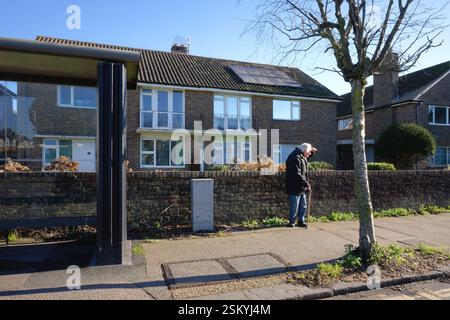 An elderly man with white hair and walking stick looking into the distance while waiting on a suburban road in Worthing West Sussex England UK Stock Photo