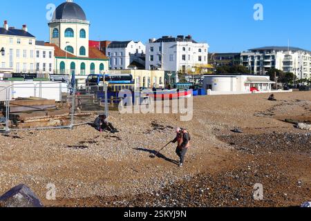 A man using a metal detector on the east beach at Worthing on a sunny winters day West Sussex England UK Stock Photo