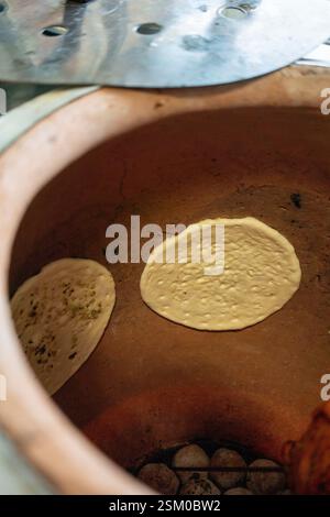 Baking naan breads on the hot walls of a tandoor oven, highlighting a traditional cooking method from South, Central, and West Asia Stock Photo