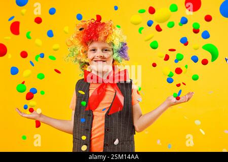 Happy boy dressed like clown and confetti on orange background. Party time Stock Photo