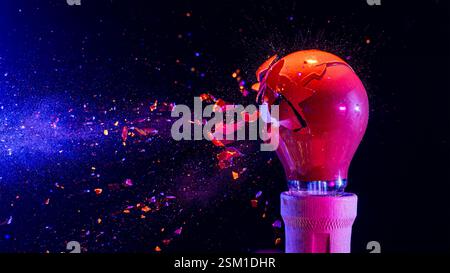 Red light bulb exploding dramatically with shards flying through the air, creating a vibrant display of destruction and energy Stock Photo