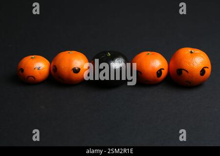 Stop racism. One black tangerine among orange ones on black background, closeup Stock Photo