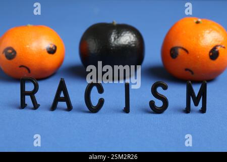 One black tangerine among orange ones and word Racism made with beads on blue background, closeup Stock Photo