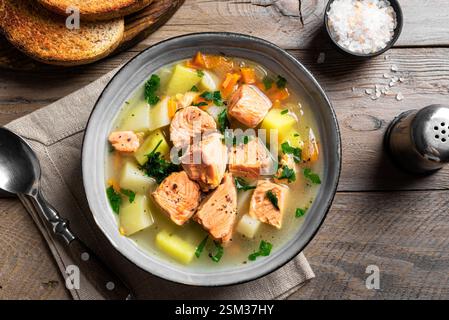 Salmon fish soup isolated on wooden table. Traditional homemade soup with red salmon and vegetables. Stock Photo