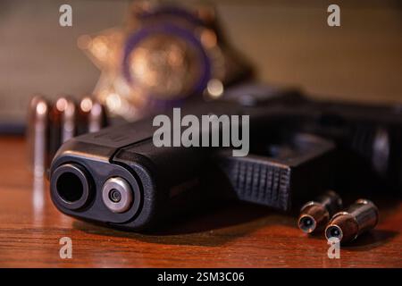 A black semi-automatic handgun rests on a table with hollow point ammunition. A law enforcement badge and more bullets can be seen in the background. Stock Photo