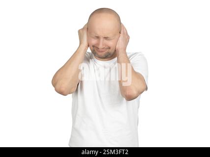 A bald Caucasian man with light stubble is wearing a white t-shirt and covering his ears with both hands. Stock Photo