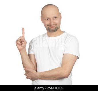 A bald Caucasian man with a short beard is wearing a white t-shirt and smiling while pointing upwards with his index finger. Stock Photo