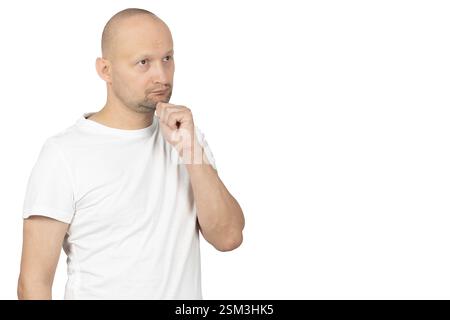 A bald Caucasian man in a white t-shirt stands against a plain white background, touching his chin while looking upward in deep thought. Stock Photo
