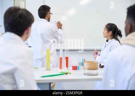 Chemistry teacher explaining chemical formula on whiteboard to students Stock Photo