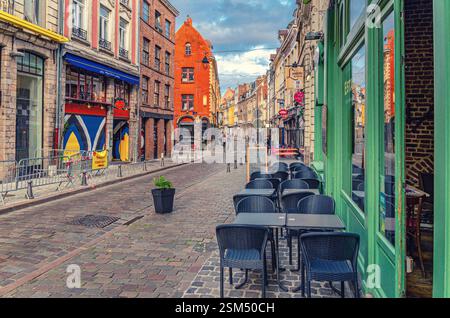 Lille, France, July 3, 2023: Street restaurant with tables and chairs on narrow cobblestone street, empty road with paving stone, old colorful buildin Stock Photo
