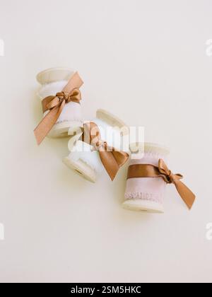 Three spools of ribbon in pastel colors with matching bows sit elegantly on a neutral background, ideal for crafting. Stock Photo