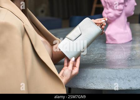 Sophisticated woman presenting stylish, beige, leather wallet at dining, elegant, setting, accessory, fashion, concept Stock Photo