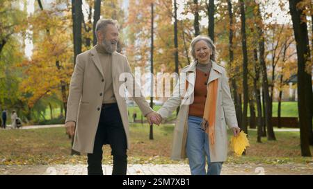 Middle aged 60s couple gray-haired wife and husband in elegant outerwear walking romantic date in autumn city park Caucasian happy family woman man Stock Photo
