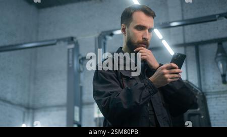 Male guy mechanic Caucasian adult man engineer technician industrial worker electrician in uniform using mobile phone think thoughtful typing Stock Photo