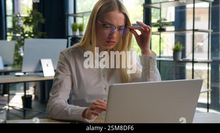 Caucasian businesswoman girl office manager confused business woman working laptop eyestrain problem take off glasses blurry vision bad eyesight Stock Photo