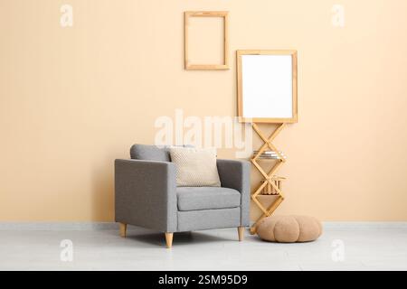 Armchair with pouf, shelves and photo frames on beige wall Stock Photo