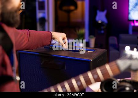 Sound engineer adjusting volume levels on his amplifier to record acoustic guitar tunes for editing session in music post production. Male producer composing a new song in home studio. Close up. Stock Photo