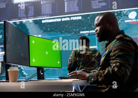 Military expert handles satellite cctv data next to mockup screen, working in a base of operations with high tech gear to support important defense missions. Coordinates strategic tactics. Stock Photo