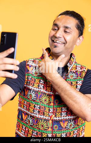 Cheerful man using cellphone to take selfies, rubbing chin. Smiling social media user taking photos using phone selfie camera, doing ego stroking hand gesturing, studio background Stock Photo