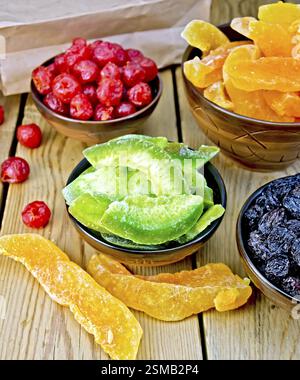 Candied pomelo, cantaloupe, cherries, raisins in bowls, paper bag on a wooden boards background Stock Photo