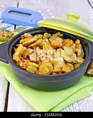 Jerusalem artichokes roasted in a roasting pan with a lid, fresh tubers on a napkin, the meter and pills on a white background wooden plank Stock Photo