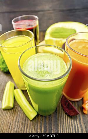 Four tall glasses with the juice of carrot, cucumber, beetroot and pumpkin with vegetables on the background of wooden boards Stock Photo