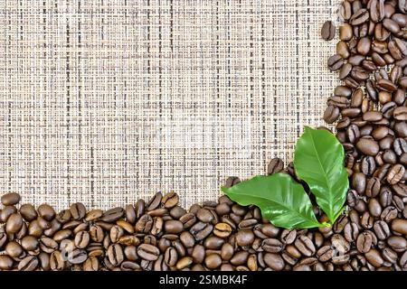Frame of black coffee beans with leaves on brown coarse woven fabric Stock Photo