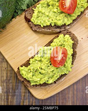 Two slices of rye bread with tomato and guakomole, napkin, avocado on the background dark wooden boards Stock Photo