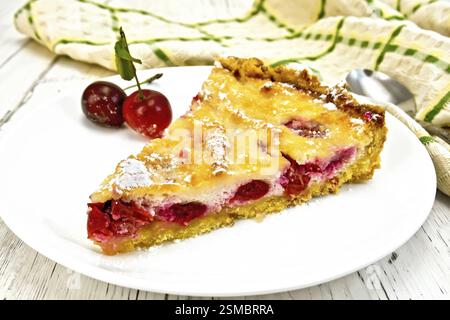 Pie with cherries and sour cream in a dish, kitchen towel with a spoon on a background of wooden boards Stock Photo