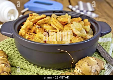 Jerusalem artichokes roasted in a roasting pan, fresh tubers on a napkin, the meter and pills on the background of wooden boards Stock Photo