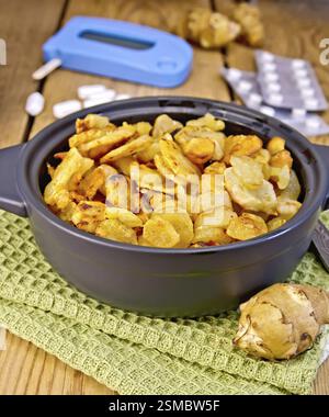 Jerusalem artichokes roasted in a roasting pan, fresh tubers of Jerusalem artichoke on a napkin, the meter and pills on the background of wooden board Stock Photo