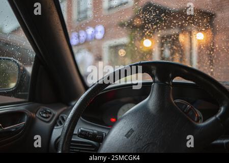 View from inside a car with raindrops on the window and a blurred view of lights outside Stock Photo