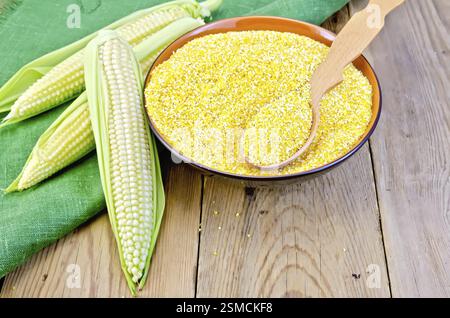 Corn grits in a bowl with a spoon, corn on the cob on a green napkin on the background of wooden boards Stock Photo