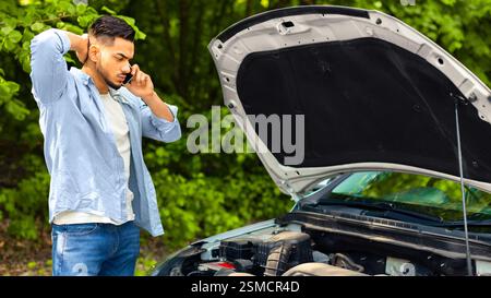 Sad arab man looking at engine and calling auto service Stock Photo