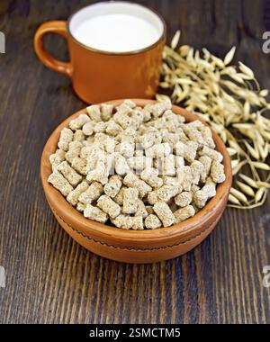 Oat bran large in earthenware bowl, a mug with milk, oat stalks on a wooden boards background Stock Photo
