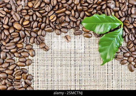 Frame of black coffee beans with green leaves on brown coarse woven fabric Stock Photo