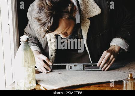 A man using a measuring tool on wood, showing focused craftsmanship Stock Photo