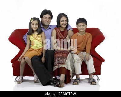 South Asian Indian family with father mother son and daughter sitting on sofa smiling and looking at camera MR . 698, 699, 700, 701 Stock Photo